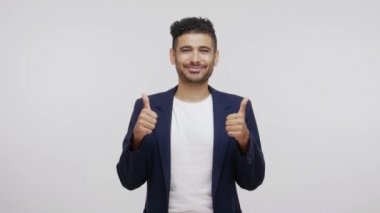 Zarif takım elbiseli, mutlu bir ifadeyle kameraya bakan, işi onaylayan, gönderileri seven mutlu, mutlu sakallı bir adam. Gri arka planda izole edilmiş kapalı stüdyo görüntüleri