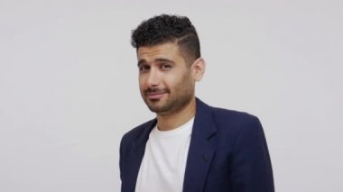Takım elbiseli yakışıklı sakallı adam kameraya iyimser bir gülümsemeyle bakıyor flört ediyor, randevu istiyor. Gri arka planda izole edilmiş kapalı stüdyo görüntüleri