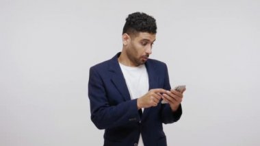 Sakallı adam akıllı telefon üzerinde çalışıyor ve kameraya heyecanlı bir ifadeyle bakıyor, kolay bankacılığa, online alışverişe ve bahislere şaşırıyor. Gri arka planda izole edilmiş kapalı stüdyo görüntüleri