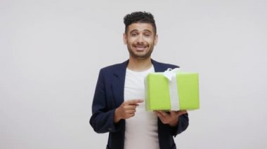 Bu hediye senin için. Cömert sakallı adam elinde kocaman yeşil hediye kutusuyla hediye veriyor, tebrik ediyor. Gri arka planda izole edilmiş kapalı stüdyo görüntüleri