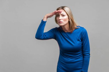 Zarif, dar, mavi elbiseli, güzel, hırslı bir kadının portresi. Geleceği dört gözle bekliyor. Gri arka planda kapalı stüdyo çekimi