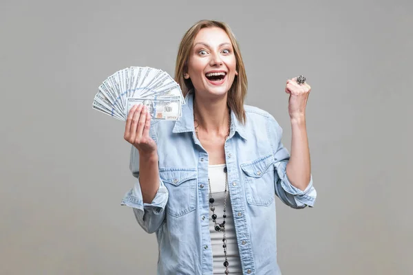 ドルのファンを持つデニムシャツの中で非常に幸せな女性の肖像画 歯で笑って はい私は大きな収入を祝う ジェスチャーをしたことを示しています グレーの背景に隔離された屋内スタジオで — ストック写真