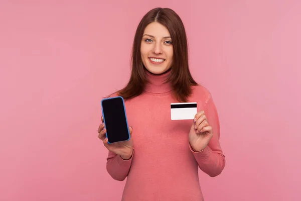 분홍색 스웨터를 카드와 휴대폰을 카메라에 미소를 온라인 사용하는 여자의 스튜디오 — 스톡 사진