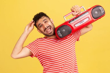 Çizgili kırmızı tişörtlü, omuzlarında kırmızı bant kayıt cihazı olan ve müzik dinlemekten zevk alan son derece mutlu bir adam. Sarı arka planda kapalı stüdyo çekimleri