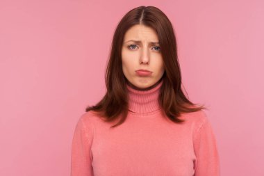 Pembe kazaklı, hayal kırıklığına uğramış esmer kadının yakından çekilmiş bir portresi, hayal kırıklığı. Pembe arka planda kapalı stüdyo çekimleri