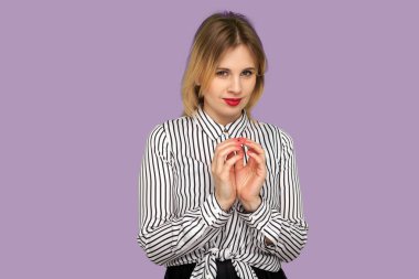 Scheming sly woman with beautiful red lips in striped blouse smirking at camera, thinking over devious plan with cunning expression, bitchy look. indoor studio shot isolated on purple background