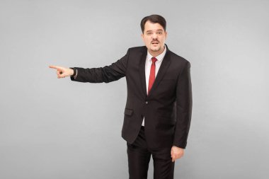 Kovuldun, bu son hataydı. Kapalı stüdyo çekimi. Gri arka planda izole. Siyah takım elbiseli, kırmızı kravatlı ve bıyıklı yakışıklı işadamı kameraya bakıyor..