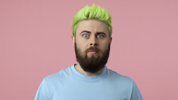 明るい緑の髪を染めと衝撃的な髭の若い男は彼の口を閉じて 誰にも何も言わないことを約束し 秘密を守る ピンクの背景に隔離された屋内スタジオショット — ストック動画