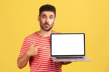 Sakallı, boş dizüstü bilgisayarı işaret eden ve büyük gözlerle kameraya bakan heyecanlı adam reklamla şok oldu. Sarı arka planda kapalı stüdyo çekimleri