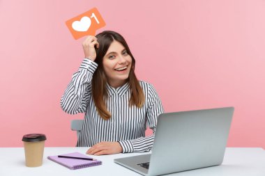 Heyecanlı blog yazarları iş yerinde dizüstü bilgisayarlarıyla oturup sosyal ağlarda yazılar yazmayı severler. Pembe arka planda kapalı stüdyo çekimleri
