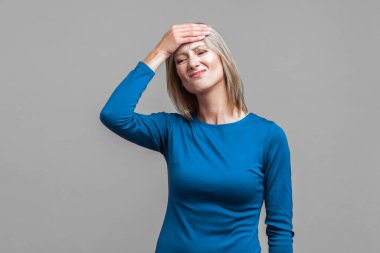 Yüz efekti, kötü hafıza kavramı. Zarif mavi elbiseli, elleri başının üstünde umutsuzca hatırlamaya çalışan üzgün bir kadının portresi. Gri arka planda kapalı stüdyo çekimi