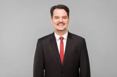 Sakallı, zarif takım elbiseli yakışıklı iş adamı bıyıklı, dişlek gülüşlü bir ifadeyle kameraya bakıyor. Başarılı bir CEO ya da komisyoncu. Gri arkaplanda izole.