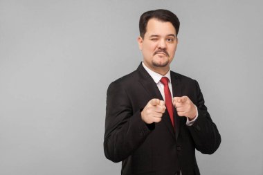 Hey sen, senden hoşlanıyorum! Bir adam sana göz kırpıyor ve flört ediyor. Stüdyo içi çekim, gri arka planda izole edilmiş. Siyah takım elbiseli, kırmızı kravatlı ve bıyıklı yakışıklı iş adamı kameraya bakıyor.