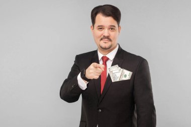 Yakışıklı iş adamı küçük bir gülümsemeyle kamerayı işaret ediyor. İçerde, stüdyoda, gri arka planda izole edilmiş.