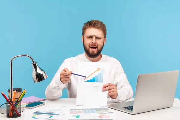 Excited nervous man office worker showing paper with diagram, pointing at increasing arrow, worried about sharp rise in prices. Indoor studio shot isolated on blue background.