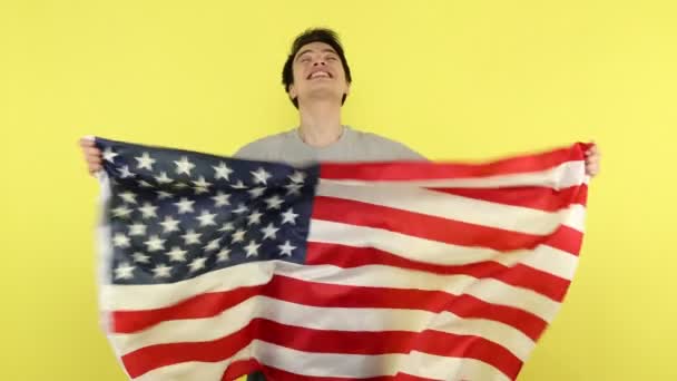 大きなアメリカ国旗を手にした非常に幸せな若い男が心から喜び 彼の米国への移動 愛国心を祝う 黄色の背景に隔離された屋内スタジオショット — ストック動画