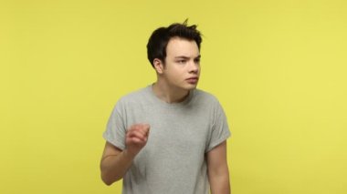 Gri tişörtlü meraklı genç adam kulağının yanında elini tutuyor ve dikkatlice dinliyor. Özel konuşmalarını duymaya çalışıyor. Sarı arka planda kapalı stüdyo çekimleri