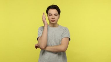 Gri tişörtlü sıkkın bir genç, kafa üstü eğip sıkıcı konuşmaları dinliyor, duygusuz duygular, tembellik ve enerji eksikliği. Sarı arka planda kapalı stüdyo çekimleri