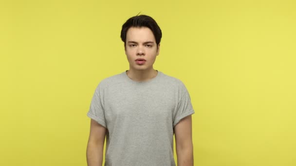 灰色のTシャツの若い男は 小さなサイズに不満を少しジェスチャーを示し 低レートの指で最小限の記号を行う 黄色の背景に隔離された屋内スタジオショット — ストック動画
