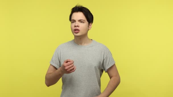 カジュアルなスタイルの灰色のTシャツの若い男が話している間 喉の痛みを感じ 首の不快感 炎症を心配し 扁桃腺を麻痺させる 黄色の背景に隔離された屋内スタジオショット — ストック動画