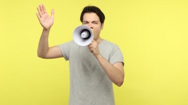 Duygusallık taslayan, gri tişörtlü, haber yayan, megafonla konuşan, aktif olarak el kol hareketi yapan genç adam, öğrenciler grev yapıyor. Sarı arka planda kapalı stüdyo çekimleri