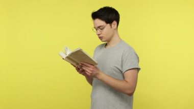 Gözlüklü zeki genç bir öğrenci ve sıradan tarz gri tişört giyen, baş parmak gösteren, senaryoyla tatmin olmuş bir kitap okuyan. Sarı arka planda kapalı stüdyo çekimleri