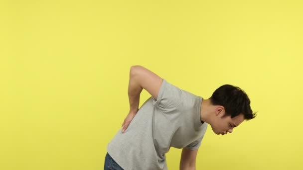 不幸な働き過ぎの若い男が腰痛に苦しみ まっすぐにしようとし 耐え難い痙攣 腎臓結石 松葉杖神経に触れている 黄色の背景に隔離された屋内スタジオショット — ストック動画