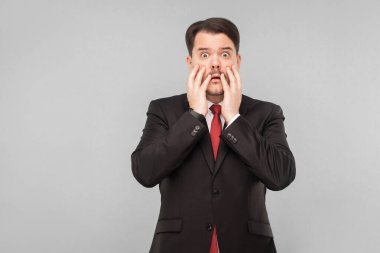 Stresli bir iş adamı kameraya bakıyor, yüzünü ellerle kapatıyor ve borsadaki hisselerin düştüğüne ve bitcoin 'in büyüdüğüne inanamıyor. Stüdyo. Gri arkaplanda izole