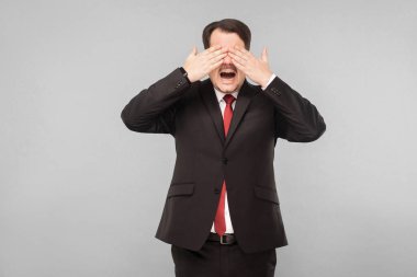 Gözlerini kapadı ve yüze kadar saydı. İş yerinde saklambaç oynarız. Kapalı stüdyo çekimi. Gri arka planda izole. Siyah takım elbiseli, kırmızı kravatlı ve bıyıklı yakışıklı bir iş adamı.