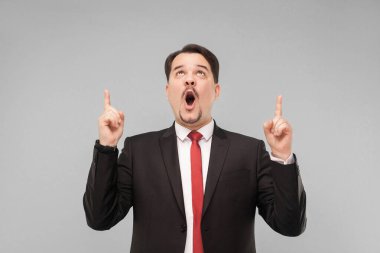 Duygusal adam parmağını kaldırıyor. Bu bir iskonto değil. Kapalı stüdyo çekimi. Gri arka planda izole. Siyah takım elbiseli, kırmızı kravatlı ve bıyıklı yakışıklı işadamı yukarı bakıyor..