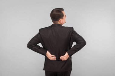 Kötü duygular konsepti. İş adamının sırtı ağrıyor. İçerde, stüdyoda, gri arka planda izole edilmiş.