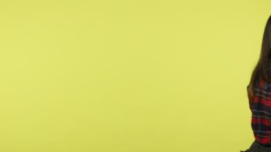 Sırtında dört tane kağıt kahve fincanı taşıyan mutlu esmer kadın öne doğru yürüyor ve gülümsüyor, eğleniyor, teslimat yapıyor. Sarı arka planda kapalı stüdyo çekimleri