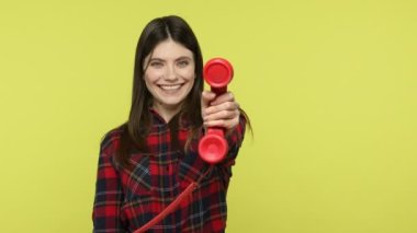 Ara beni! Kırmızı telefon ahizesi tutan, kameraya gülümseyen ve iletişim teklif eden, kareli gömlekli mutlu esmer kız. Sarı arka planda kapalı stüdyo çekimleri