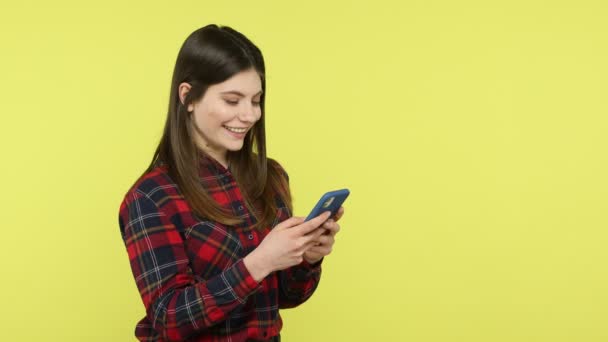 Mujer Joven Alegre Camisa Cuadros Sinceramente Sonriendo Escribiendo Teléfono Inteligente — Vídeos de Stock