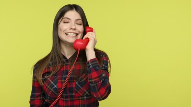 小切手シャツに赤い携帯電話を保持固定電話の話でかなりブルネットの女性は 食品の配達を注文し 友人に 通信を呼び出す 黄色の背景に隔離された屋内スタジオショット — ストック動画