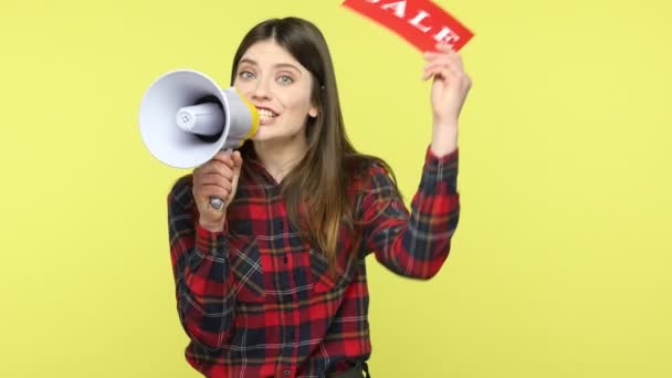 チェッカーシャツの女性プロモーターは 手に販売の碑文 広告割引とメガホン保持カードで素晴らしいニュースを発表しました 黄色の背景に隔離された屋内スタジオショット — ストック動画