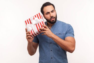 Meraklı sakallı adam çizgili hediye kutusunu sallıyor içinde ne olduğunu tahmin etmeye çalışıyor sürprizler ve ikramiyelerle merak ediyor. Beyaz arka planda izole edilmiş kapalı stüdyo görüntüleri