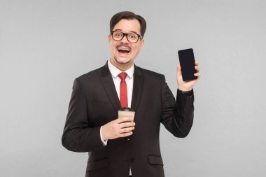 İş, aletler, teknolojiler. Adam yeni telefonu gösteriyor. İçerde, stüdyoda, gri arka planda izole edilmiş.