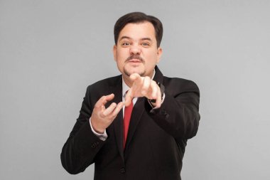 Komik işçi kameraya bakıp şeytanmış gibi davranır, aslında kibardır. Kapalı stüdyo çekimi. Gri arka planda izole. Kırmızı kravatlı ve bıyıklı yakışıklı işadamı kameraya bakıyor..