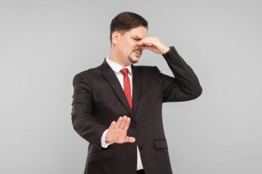 Fu, bu çok kötü kokuyor... iğrenç... kapalı alan, stüdyo çekimi, gri arka planda izole edilmiş. Siyah takım elbiseli, kırmızı kravatlı ve bıyıklı yakışıklı bir iş adamı..