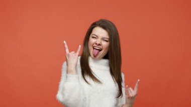Beyaz kazaklı yaramaz itaatsiz bir kadın rock 'n roll jesti sergiliyor parmakları dillerini çıkarıp çığlık atıyor ve konserde eğleniyor. Turuncu arka planda kapalı stüdyo çekimleri