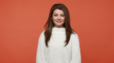 Beyaz kabarık kazaklı güzel esmer kadın ellerini birbirine bastırıyor ve gülümsüyor, sakinleşmek ve uyum ve meditasyon bulmak için yoga yapıyor. Turuncu arka planda kapalı stüdyo çekimleri