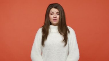 Beyaz kazak giymiş endişeli bir kadın paniğe kapılıp parmaklarını Mudra pozisyonunda bastırıyor gözlerini kapıyor ve yoga yaparken rahatlıyor. Turuncu arka planda kapalı stüdyo çekimleri