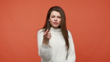 Hemen şimdi ve burada yap! Beyaz kazaklı, otoriter, ciddi bir kadın parmaklarını eğik gösteriyor, seni harekete geçmeye motive ediyor, hemen talep ediyor. Turuncu arka planda kapalı stüdyo çekimleri