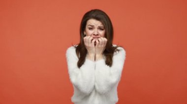 Panik içinde tırnaklarını yiyen, gergin, sabırsız esmer kadın gergin, stresli ve şaşkın bir ifadeyle bakıyor. Turuncu arka planda kapalı stüdyo çekimleri