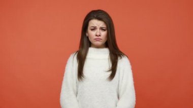 Tüylü beyaz kazaklı üzgün esmer kadın elinde facepalm hareketleriyle yüzünü kapatıyor, utangaç ve depresif, büyük bir hata yapıyor. Turuncu arka planda kapalı stüdyo çekimleri