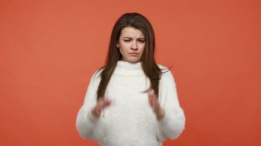 Mutsuz, hayal kırıklığına uğramış esmer kadın, stres içinde kulaklarını avuç içiyle kapatıyor, saçma sapan şeyler dinlemek istemiyor, çatışmadan kaçınmak, yüksek sesten korkmak istemiyor. Turuncu arka planda kapalı stüdyo çekimleri