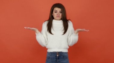 Zavallı, pofuduk beyaz kazaklı, üzgün, iflas, finansal sorunlar ve krizle kameraya bakarken boş ceplerini gösteren mutsuz esmer kadın. Turuncu arka planda kapalı stüdyo çekimleri