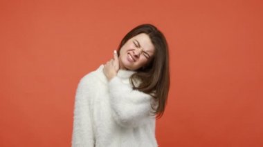 Yorgun bir kadın boynu ovuyor, oturduğu yerden sonra omuzlarına masaj yapıyor, kaslarını ısıtıyor ve gevşetiyor, iyi hissetmiyor. Turuncu arka planda kapalı stüdyo çekimleri