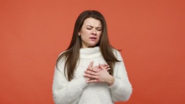 Kalp sorunları var. Mutsuz, üzgün, soluk benizli, beyaz kazaklı bir kadın. Akut ağrı, enfarktüs semptomu yüzünden kalp krizi geçiriyor. Turuncu arka planda kapalı stüdyo çekimleri